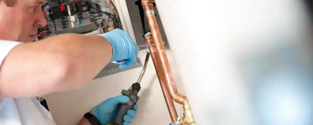 Water heater repair technician testing copper pipe connections and controls in Reno, NV
